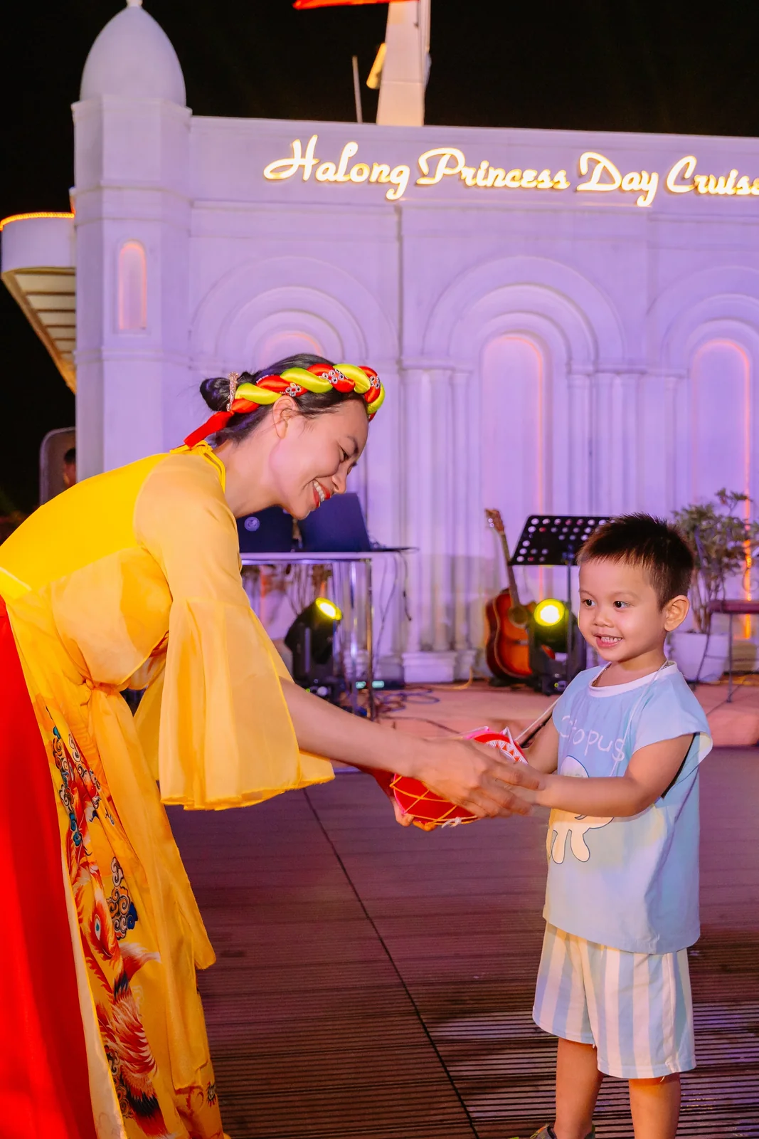 Nghệ sĩ áo tứ thân vàng trao quà lưu niệm cho một bé trai trong minishow Tinh Hoa Văn Hóa Việt trên du thuyền Hạ Long Princess