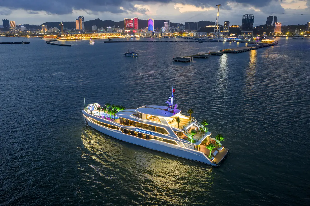 Du thuyền Catherine Horizon trên Vịnh Hạ Long với thành phố lên đèn phía sau