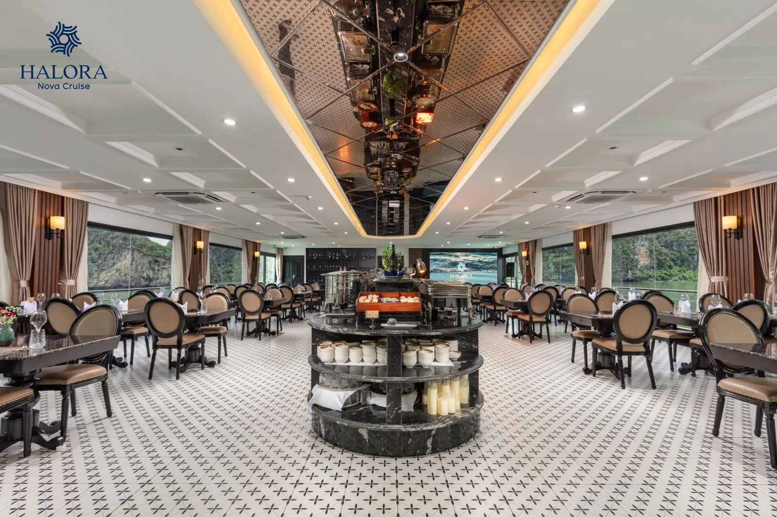 Nhà hàng chính rộng rãi với quầy buffet trung tâm cẩm thạch đen, trần gương phản chiếu tinh tế cùng dãy bàn ăn phủ khăn sang trọng, view thẳng ra vịnh Lan Hạ qua khung cửa kính lớn.