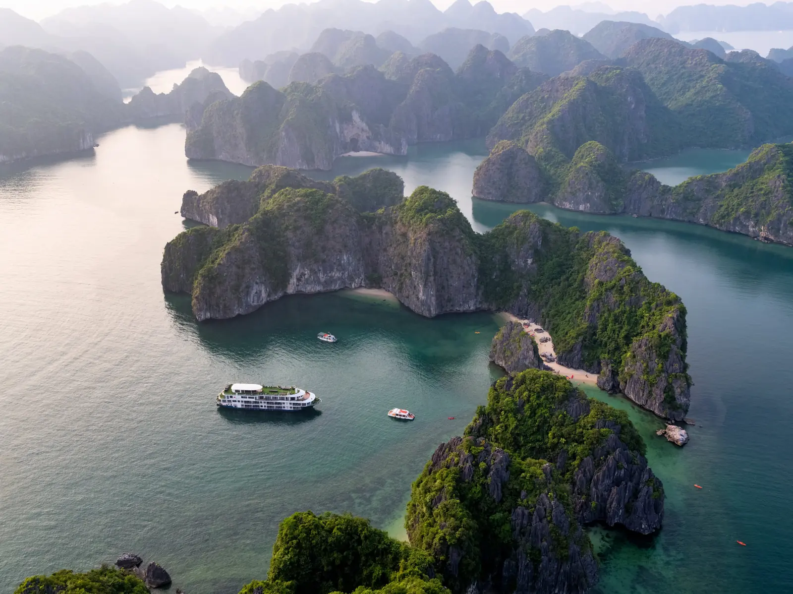 Du thuyền Mon Chéri 2 neo gần bãi biển nhỏ giữa núi đá vôi, tàu tender và khách chèo kayak gần bờ
